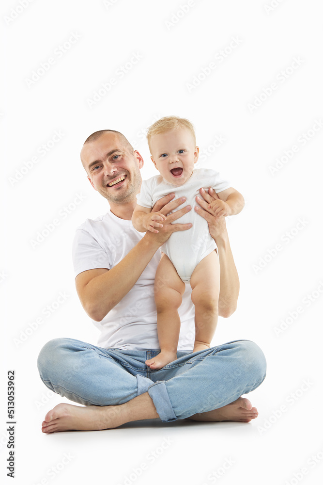 A young dad plays with a baby on a light studio background. Family values