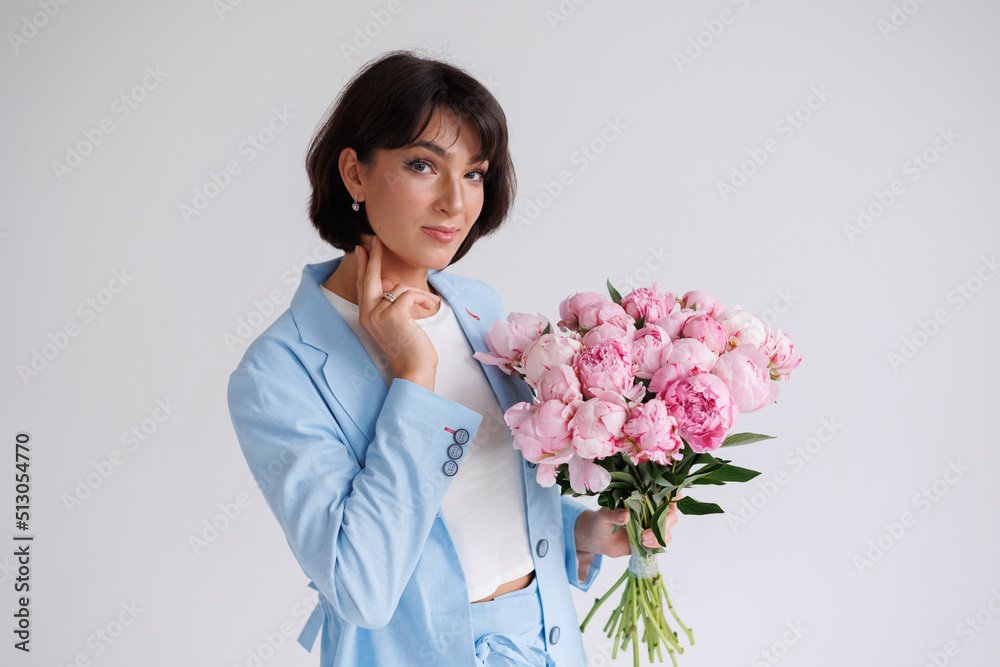 Beautiful brunette woman with short hair with bouquet of pions. Young girl with flowers. Portrait isolated. Pretty girl in blue suit smiling. Happy woman posing with flowers. Beautiful brunette woman with short hair with bouquet of pions. Young girl with flowers. Portrait isolated. Pretty girl in blue suit smiling. Happy woman posing with flowers.