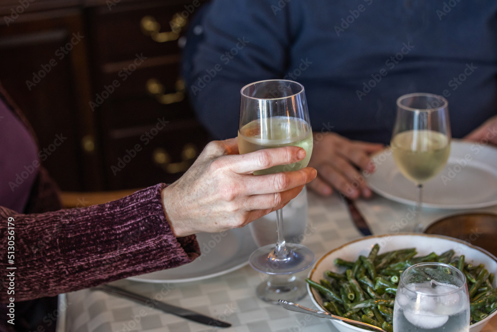A celebratory toast of white wine at a home dinner by a man and a woman with a set table and green beans nearby