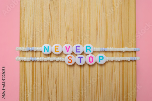 a beaded bracelet with the inscription never stop on a pink background with a copy space.