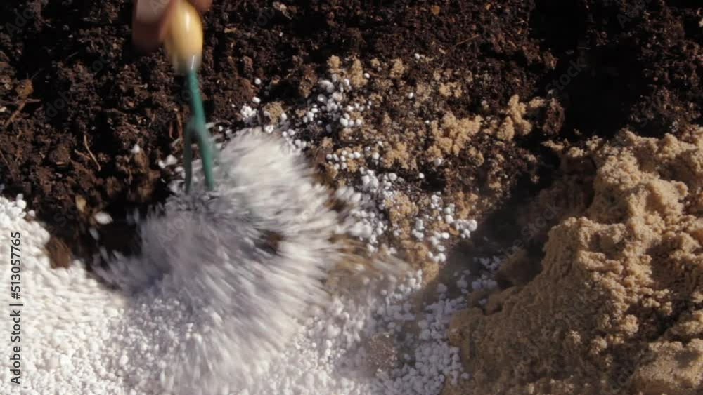 Gardening and lifestyle. closeup view of a gardener's hands with gloves, mixing soil made of sand, black earth and perlite, with a small rake in the garden. Gardening and lifestyle. closeup view of a gardener's hands with gloves, mixing soil made of sand, black earth and perlite, with a small rake in the garden.