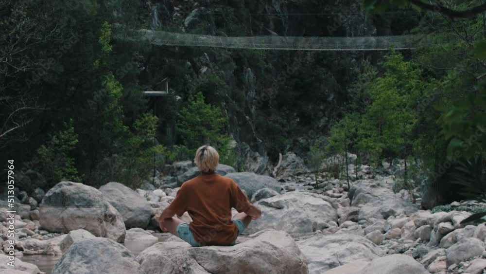 A young man sitting on the rock surrounded by forest and meditating A young man sitting on the rock surrounded by forest and meditating