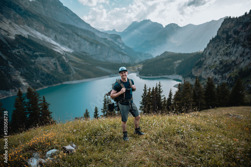 Un homme randonneur qui est en montagne lors d'une randonnée et qui regarde le magnifique panorama, avec un lac, des chemins et une forêt.