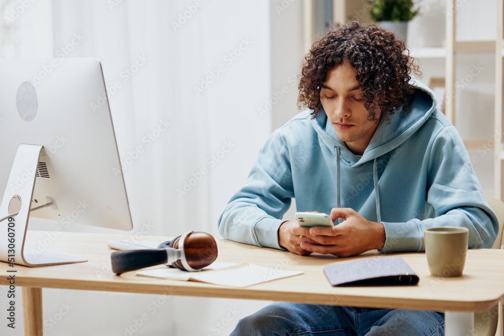 guy with curly hair in a blue jacket in front of a computer with phone Lifestyle guy with curly hair in a blue jacket in front of a computer with phone Lifestyle