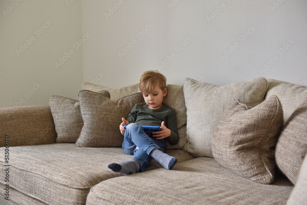 Boy sitting on the sofa at home and playing tablet Boy sitting on the sofa at home and playing tablet