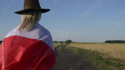 Girl in Poland flag with suitcase on country road in sunset