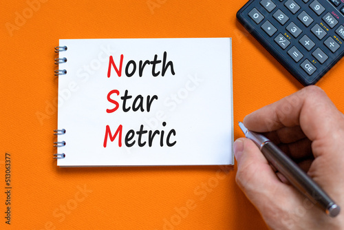 NSM north star metric symbol. Concept words NSM north star metric on white note on a beautiful orange background. Businessman hand. Business and NSM north star metric concept. Copy space. photo