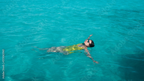 young woman in a one-piece yellow swimsuit floats on the surface of the water. Brunette girl relaxes and bathes in the blue sea  relaxing by the sea