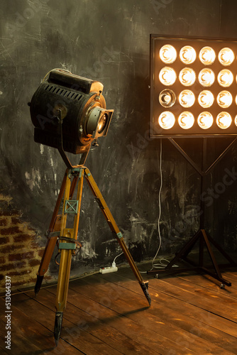 Large vintage retro spotlight in the interior in the loft style. Video movie light in the studio on stand for steampunk photo shoots. Creative photo zone, an industrial-style design element. High