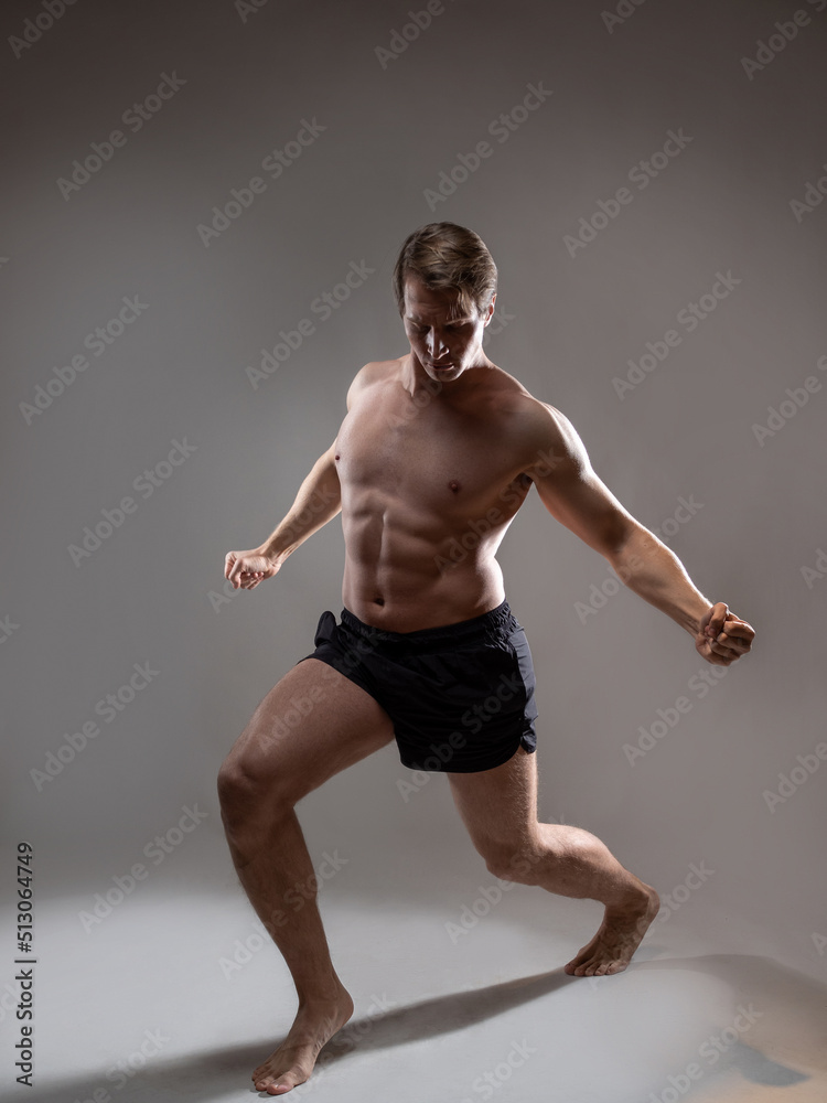 Muscular man in an artistic pose, portrait on a gray background. An athlete guy with spectacular muscles poses like an antique hero
