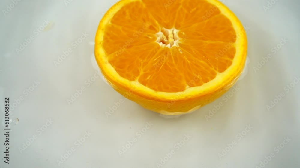 Rotating segment of a ripe and juicy orange in water on an white background. Slow motion.