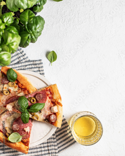 Fototapeta Naklejka Na Ścianę i Meble -  Three pieces of pizza in white plate on striped napkin, glass and basil leaves on white table. Top view