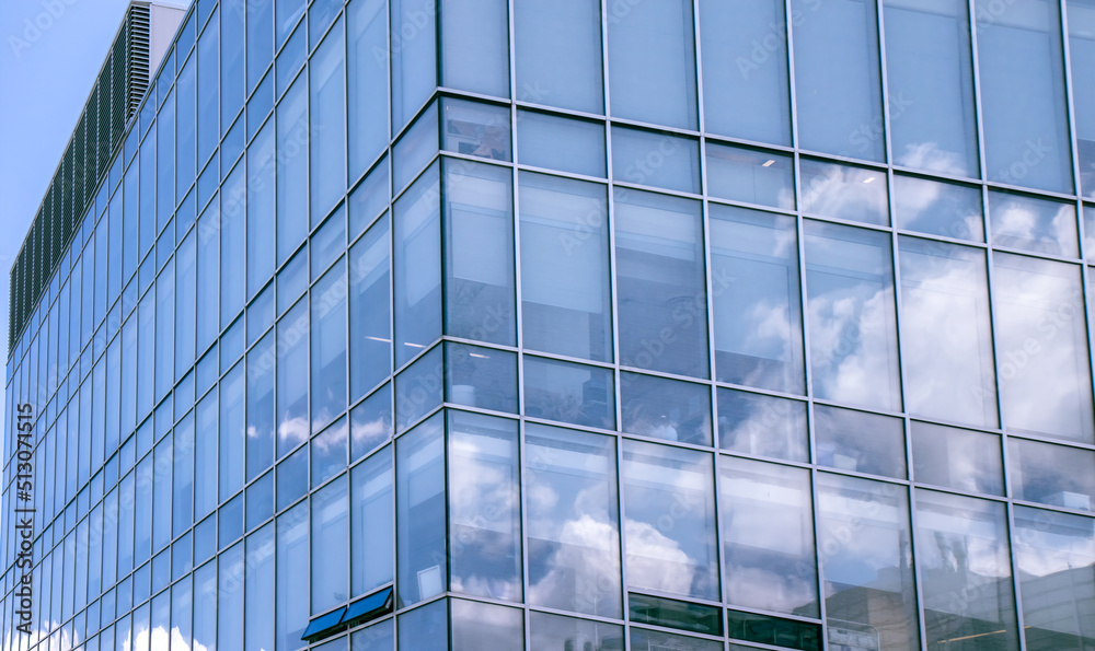 Obraz premium Exterior view of multi-storey building showing clouds reflecting in blueish window glazing, aluminum mullions, daytime, nobody