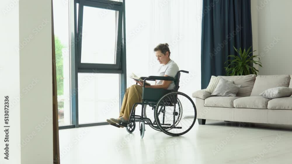 Senior woman sitting on the wheelchair reading a book at home Senior woman sitting on the wheelchair reading a book at home