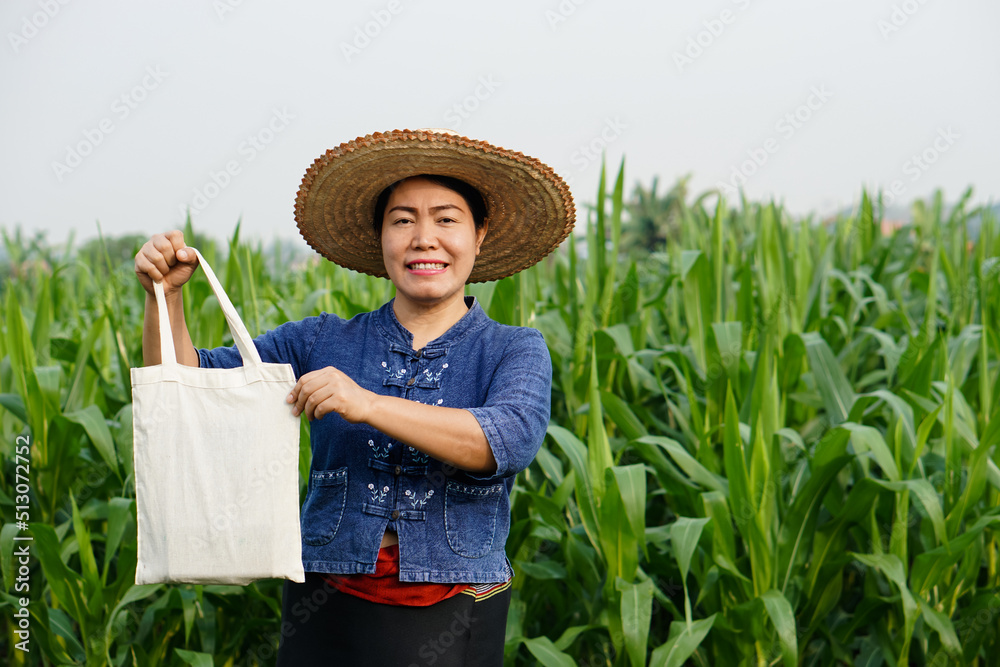 Asian woman farmer holds cotton bag ,stands at maize garden. Concept : campaign to use cotton bag instead of plastic. Reduce, reuse, recycle for environment. Earth Day.  