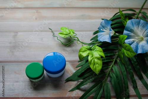 緑の植物と青い花と薬や洗剤やサプリメントの容器の写真