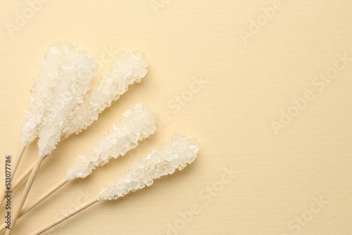 Wooden sticks with sugar crystals and space for text on beige background, flat lay. Tasty rock candies