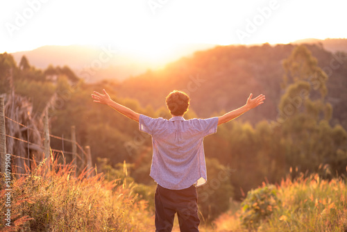 Young man with arms raised thanking God  with the sunset in the background. Concept of happiness and success.