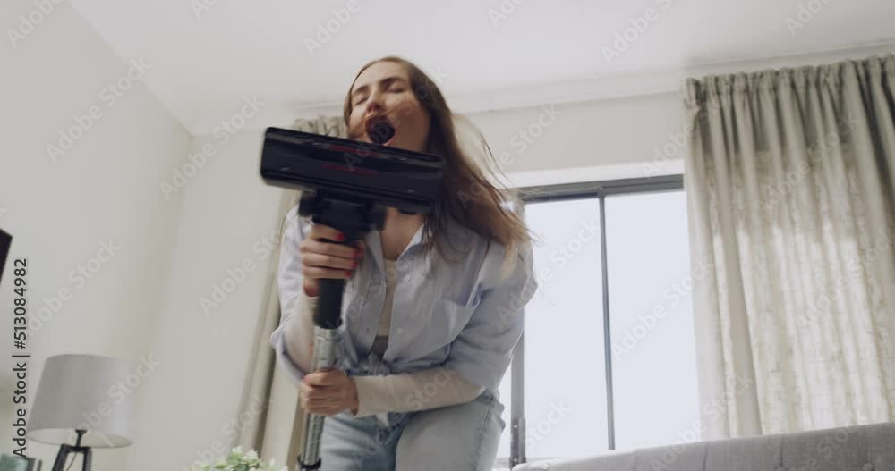 Energetic woman dancing and vacuum cleaning a carpet in a cozy living room at home. Groovy housewife singing to rock music and having fun while doing household chores and tidying up during the day Energetic woman dancing and vacuum cleaning a carpet in a cozy living room at home. Groovy housewife singing to rock music and having fun while doing household chores and tidying up during the day