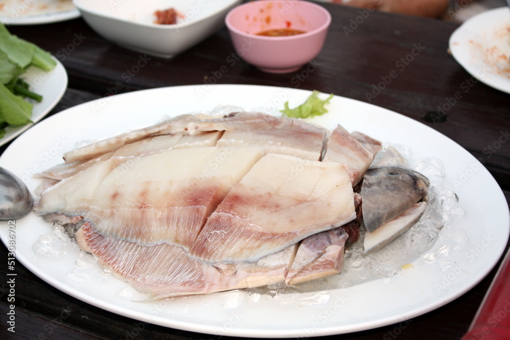 Fresh Gray pomfret, Chinese silver pomfret fish cut into pieces arranged in a white plate topped with ice. On the wooden table in the restaurant, prepare for the shabu pot. Selective focus. Fresh Gray pomfret, Chinese silver pomfret fish cut into pieces arranged in a white plate topped with ice. On the wooden table in the restaurant, prepare for the shabu pot. Selective focus.
