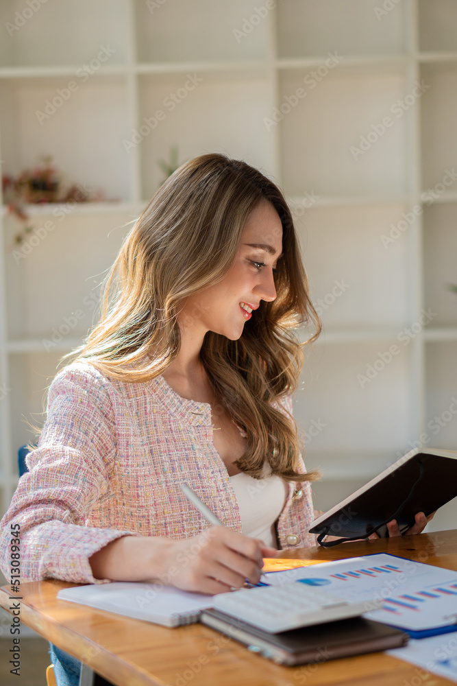 Young Asian businesswoman working on laptop computer with calculator in modern office Planning to analyze charts, business plans, investments, financial or accounting concepts. vertical picture