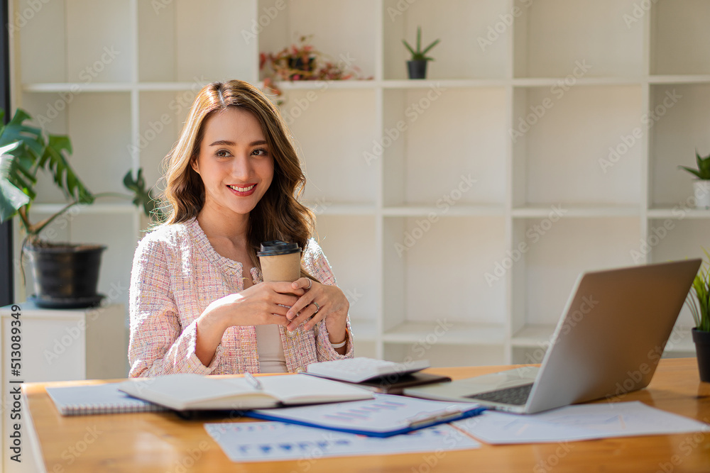 Asian businesswoman holding a cup of coffee working on investment projects and financial accounting planning strategies. Businessman talking with laptop computer at office Asian businesswoman holding a cup of coffee working on investment projects and financial accounting planning strategies. Businessman talking with laptop computer at office