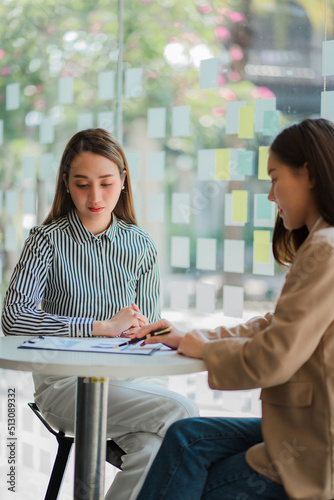 Two Asian businesswomen discussed their ideas at a meeting. Two people discuss working on investment projects and planning strategies. Businessman talking with laptop computer at office