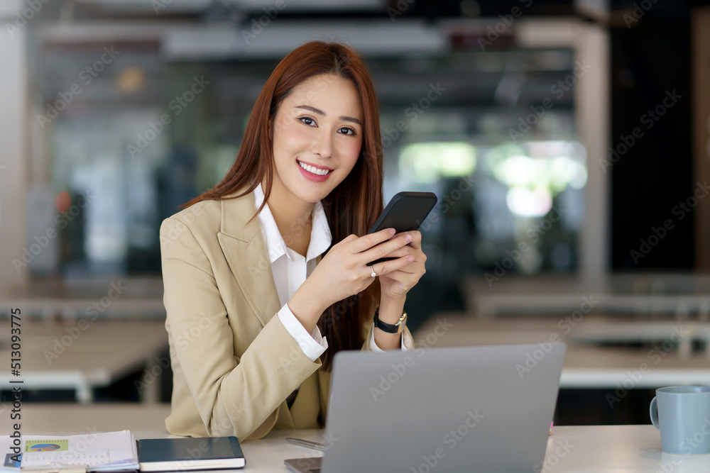 Beautiful young Asian businesswoman with a smile sitting using smartphone at the office. Beautiful young Asian businesswoman with a smile sitting using smartphone at the office.