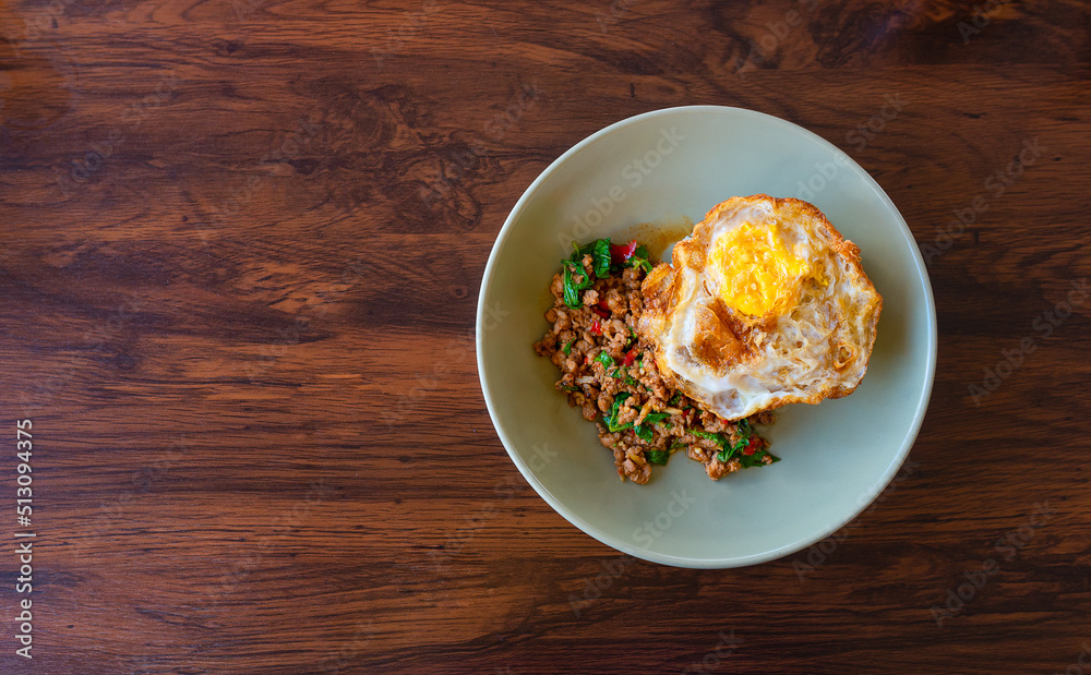 Stir fried Minced pork with basil and a fried egg on pastel plate with wooden table, Thai name is Pad kra prao Mou sub, Thailand's national dishes, famous food in Thailand.