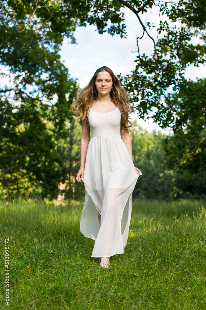 Beautiful young Russian girl dressed in a white dress, walks through the forest among the oaks in the rays of the sunset Beautiful young Russian girl dressed in a white dress, walks through the forest among the oaks in the rays of the sunset