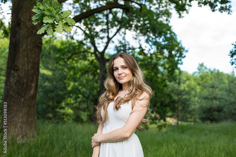 Beautiful young Russian girl dressed in a white dress, walks through the forest among the oaks in the rays of the sunset Beautiful young Russian girl dressed in a white dress, walks through the forest among the oaks in the rays of the sunset