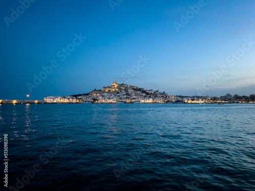 View of charming Ibiza Old town with it's castle, lit by evening lights, from the other side of the bay in Marina Botafoch. Enchanting view fora a romantic dinner for two.