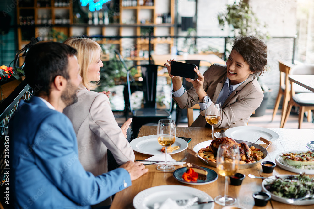 Happy businesswoman photographing her colleagues with cell phone in restaurant. Happy businesswoman photographing her colleagues with cell phone in restaurant.