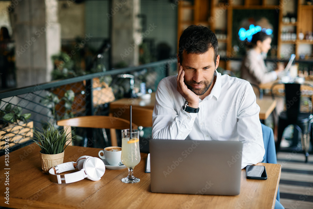 Obraz premium Smiling businessman reading e-mail on laptop in cafe.