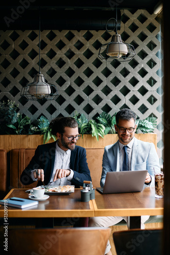 Canvas Print Happy male entrepreneurs surfing the net on laptop during breakfast in cafe