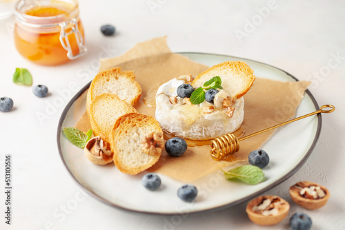 Traditional baked brie cheese or camembert with honey  nuts  blueberries and mint leaves  with breadcrumbs.