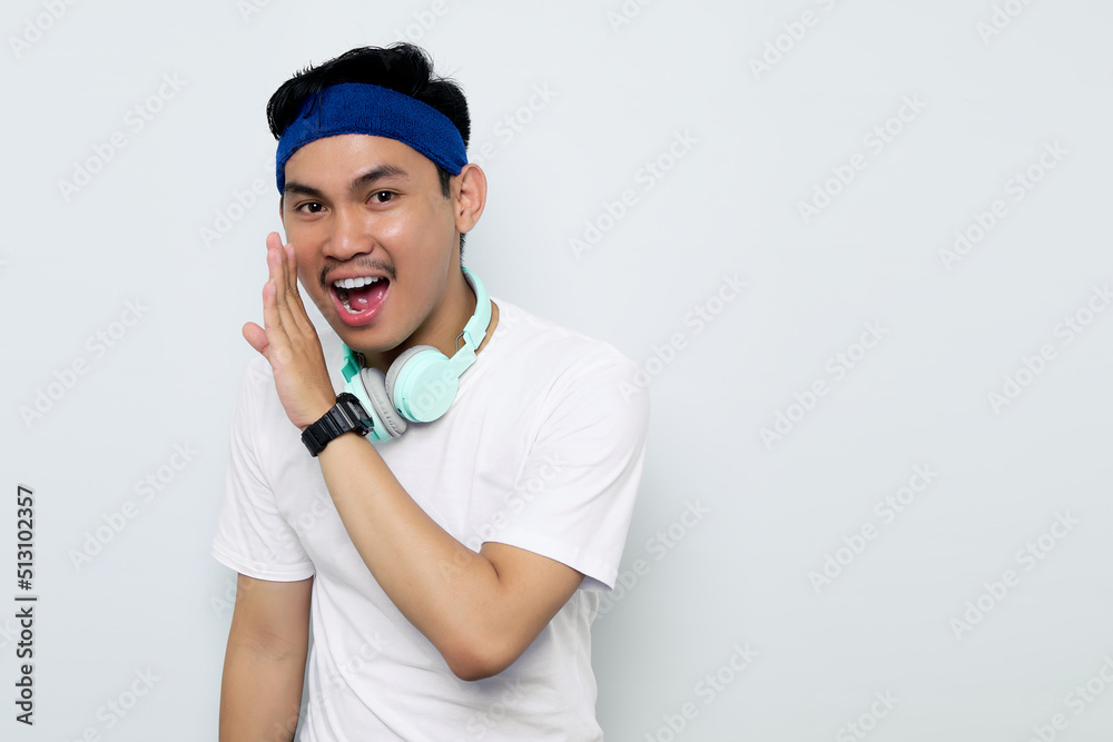 Excited young Asian sportman in blue headband and sportswear white t-shirt with headphones, whispering gossip and sharing news isolated on white background. Workout sport concept Excited young Asian sportman in blue headband and sportswear white t-shirt with headphones, whispering gossip and sharing news isolated on white background. Workout sport concept
