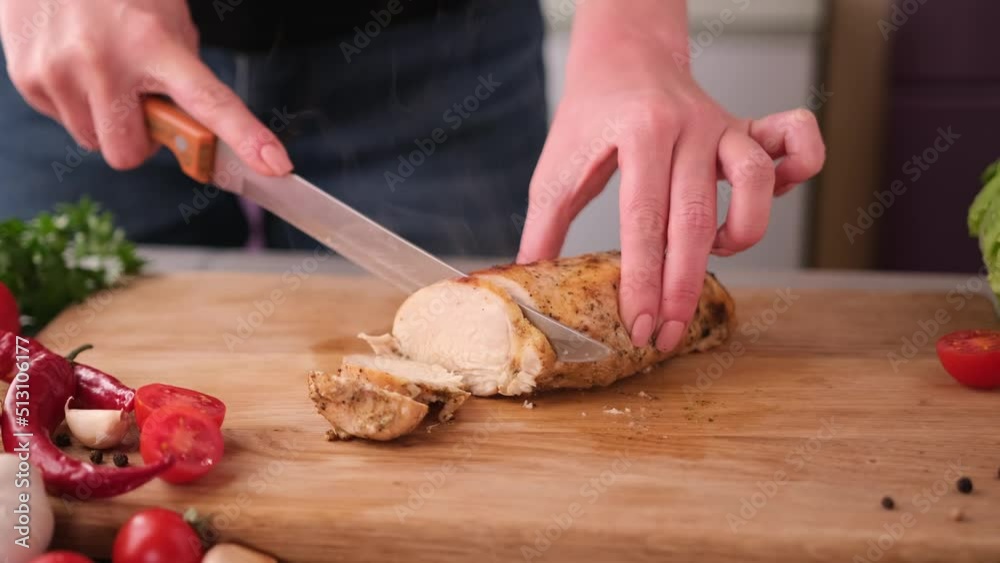 Woman cuts fried chicken breast into slices on wooden board Woman cuts fried chicken breast into slices on wooden board