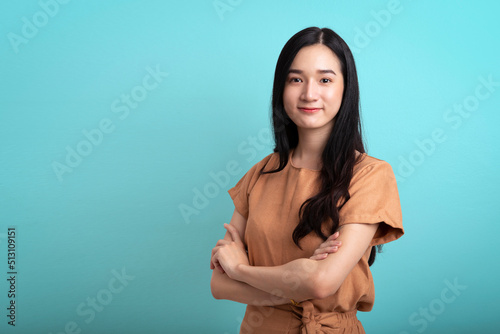 Successful young beautiful asian businesswoman cross arms confident and looking at camera smiling isolated on blue background