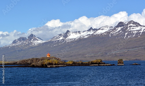 A lighthouse against the background of the Snowy peaks of the basaltic mountains of the eastern fjords in Iceland © lana
