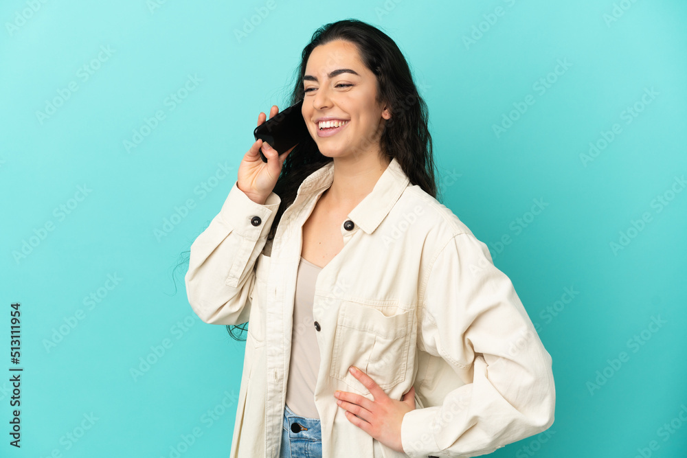 Young caucasian woman isolated on blue background keeping a conversation with the mobile phone Young caucasian woman isolated on blue background keeping a conversation with the mobile phone