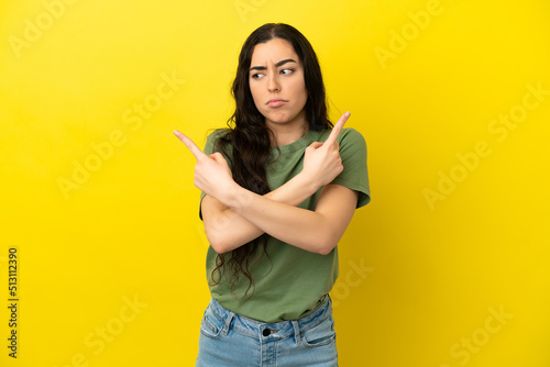 Young caucasian woman isolated on yellow background pointing to the laterals having doubts
