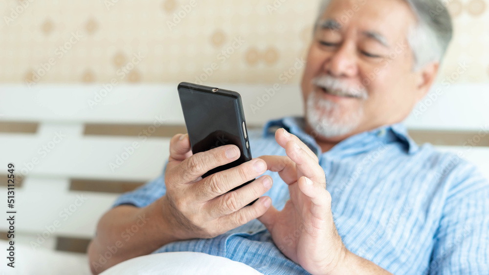 Senior Male using a smartphone , smiling feel happy in bed at home - lifestyle senior concept - select focus and blur photography Senior Male using a smartphone , smiling feel happy in bed at home - lifestyle senior concept - select focus and blur photography