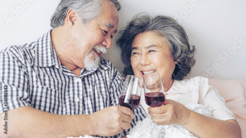 Happy love Elderly couple smile holding a wine glass , Senior couple old man and senior woman relaxing On the bed in the bedroom Celebrate the wedding anniversary - lifestyle senior concept