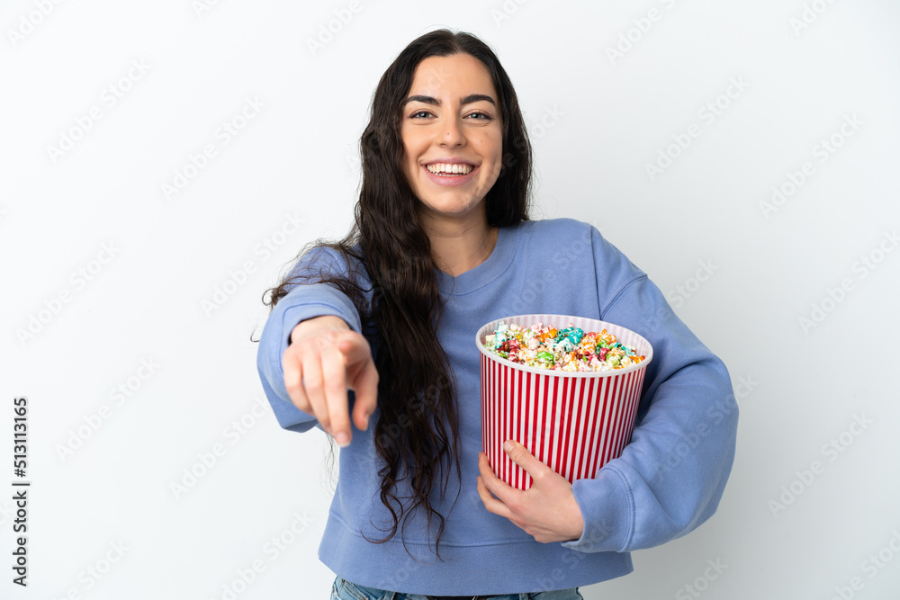 Young caucasian woman isolated on white background holding a big bucket of popcorns while pointing front Young caucasian woman isolated on white background holding a big bucket of popcorns while pointing front