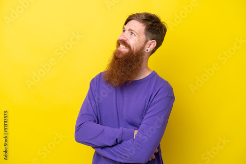 Redhead man with beard isolated on yellow background looking to the side and smiling