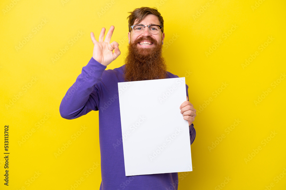 Redhead man with beard isolated on yellow background holding an empty placard and doing OK sign Redhead man with beard isolated on yellow background holding an empty placard and doing OK sign