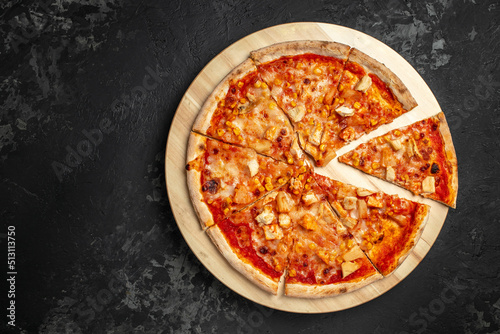 Tasty hawaiian pizza with chicken and pineapple on wooden cutting board on a dark background. food delivery, place for text, top view