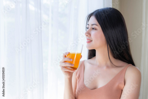 Beautiful beauty woman Asian cute girl feel happy drinking orange juice for good health in the morning , enjoying time in her home white bedroom background - lifestyle beauty woman concept
