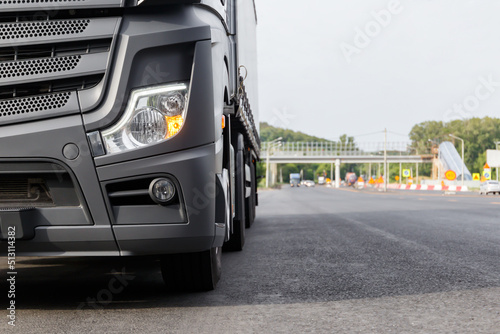 The concept of cargo transportation. A black truck is parked on the side of the highway.  Front view of a heavy truck. Front headlight close-up. A place to copy.